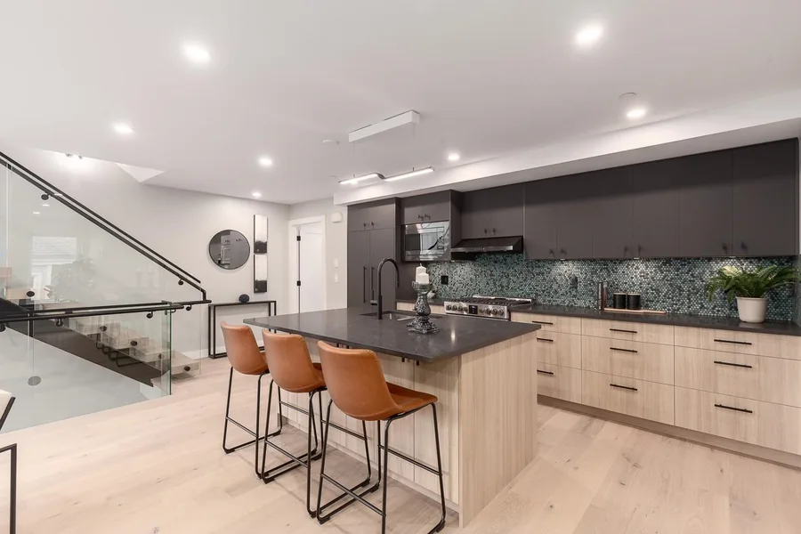 Kitchen with a dark island, light wood cabinets and leather counter stools.
