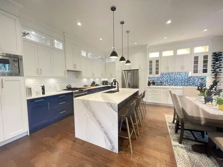 White and navy kitchen with a pale waterfall island and adjacent dining area.