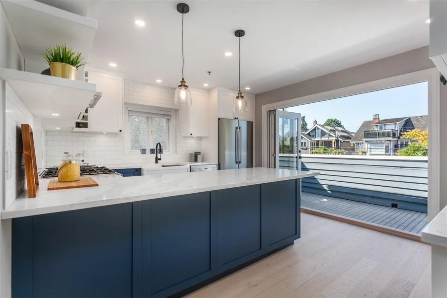 White kitchen with a deep blue island and broad patio windows.
