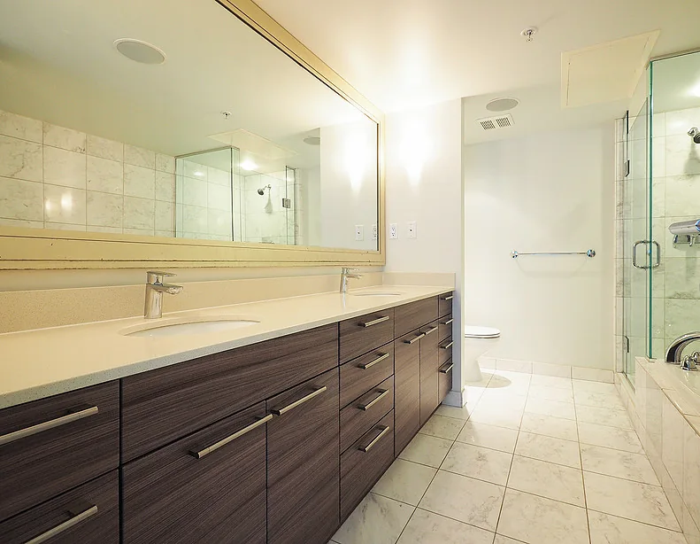 Bathroom vanity with dark drawers, a long countertop and a wall mirror.