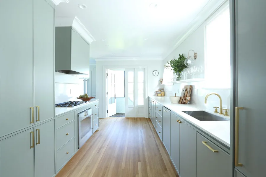 Narrow white kitchen with long work surfaces and glazed doors at the far end.