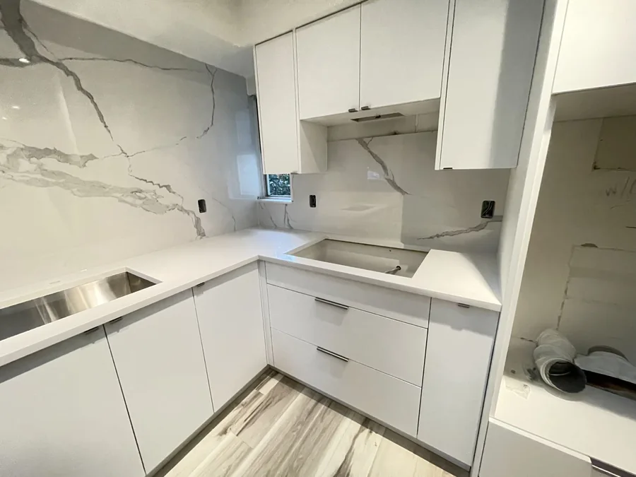 Compact white kitchen with a veined full-height backsplash and L-shaped worktop.